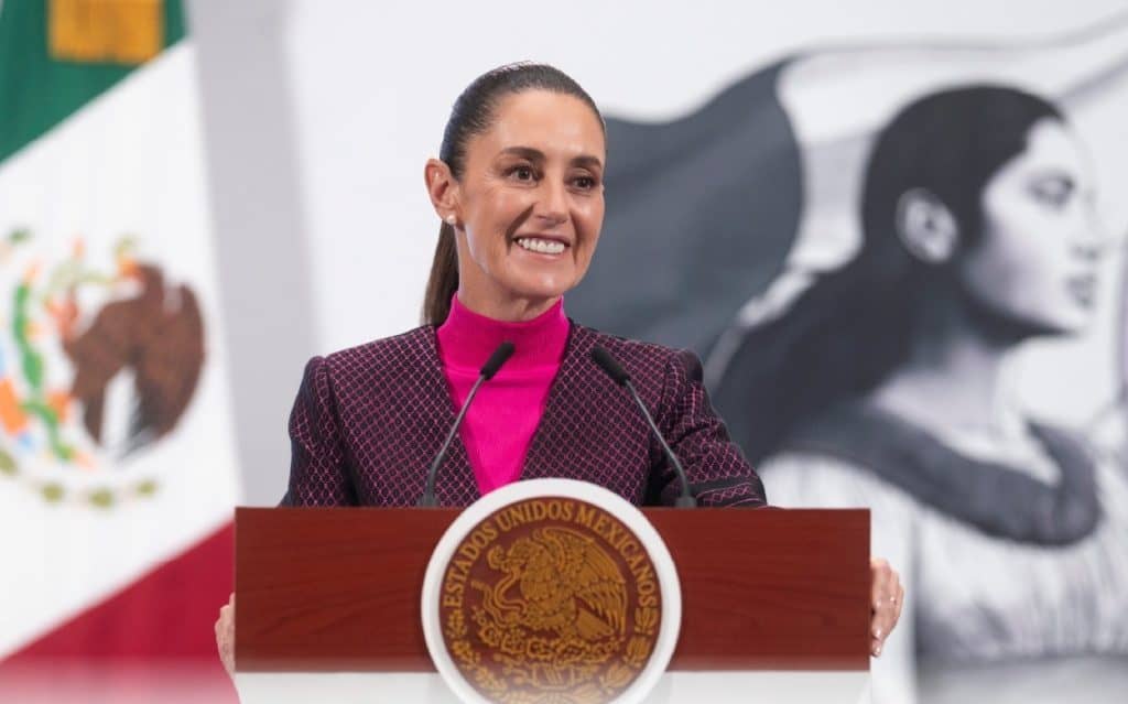 Viene de Claudia Sheinbaum a Guanajuato: inaugurará Centro de Atención de Becas en Celaya Mujer en discurso oficial en México, política, en un acto con símbolos patrios y arte moderno de fondo.