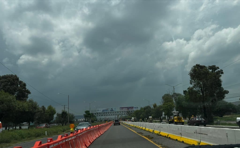 Cielo nublado sobre autopista en México, tráfico y obras en construcción, clima lluvioso.