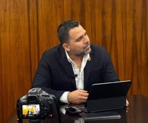 Persona en reunión laboral con laptop y cámara profesional, en fondo de madera, concepto de trabajo y negocios.