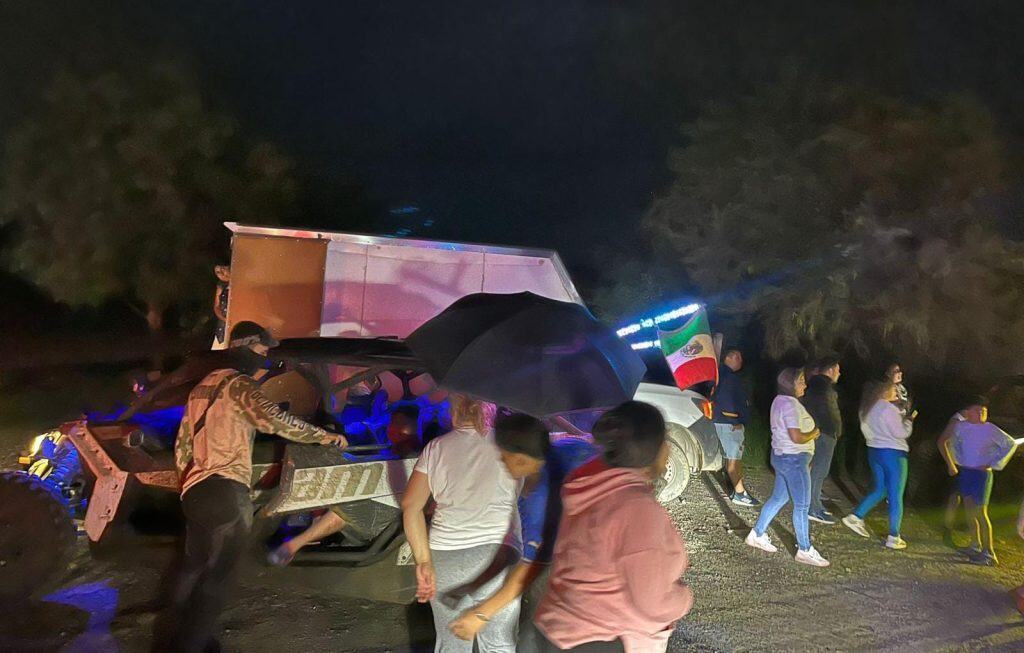 Caída de coche durante un evento nocturno con varias personas observando y bandera de México.