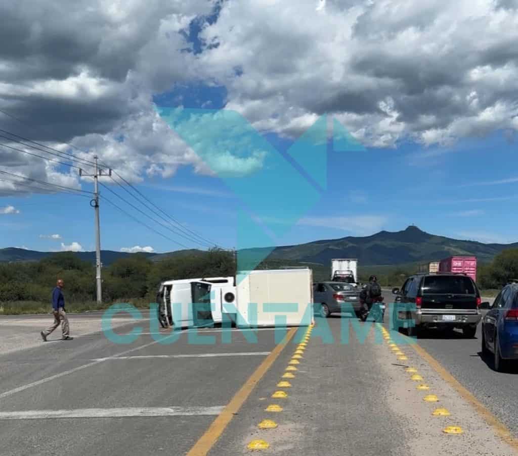 Accidente de tránsito con auto volcado en carretera, autos detenidos y paisaje montañoso de fondo.