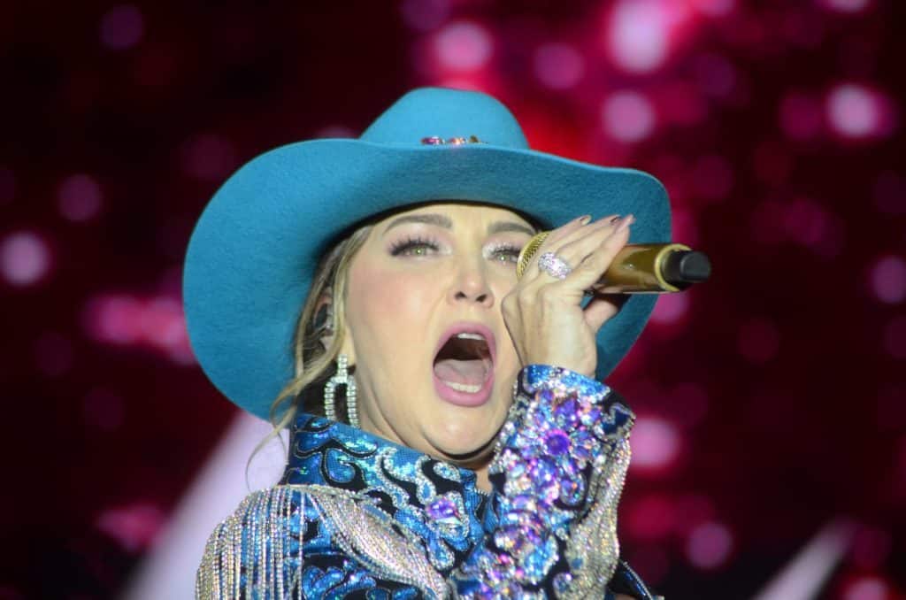 Cantante mujer con sombrero azul y vestuario brillante en escenario, realizando interpretación musical en vivo.