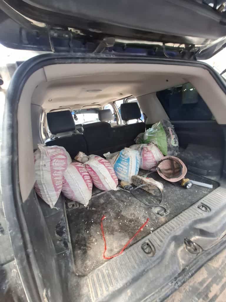 Maletero de camioneta con bolsas llenas de cemento y herramientas de construcción en interior de vehículo.