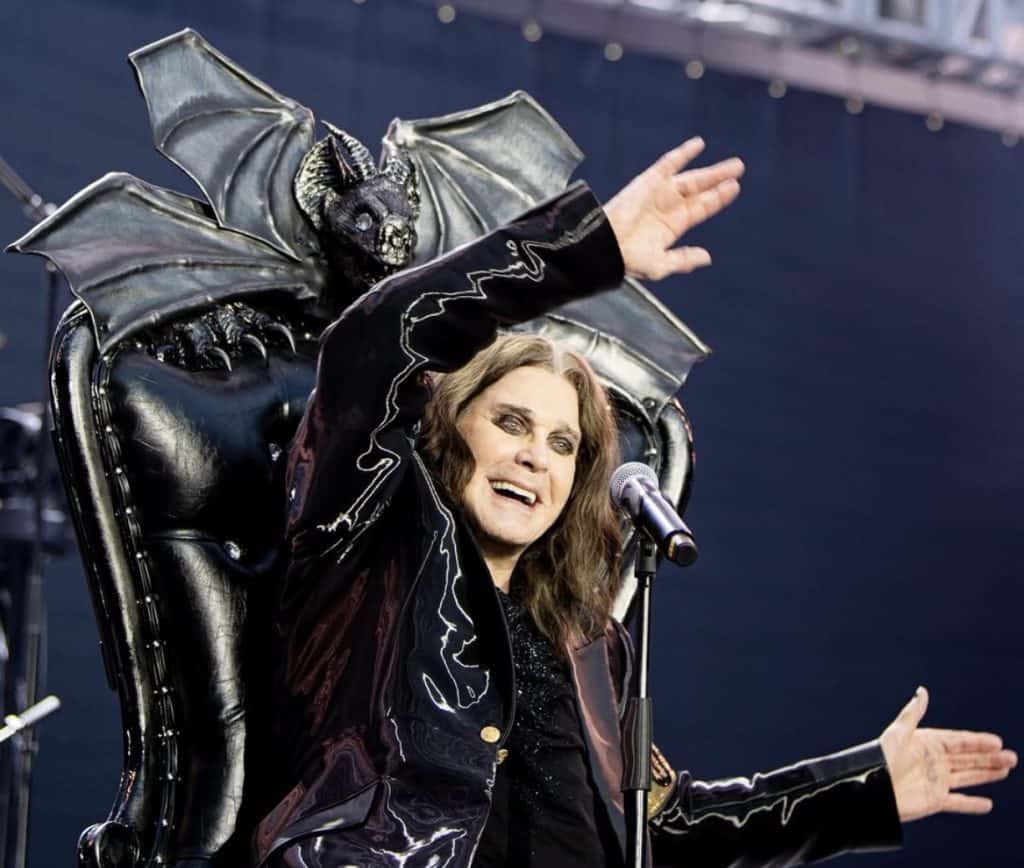 1. Escena de un cantante en escenario con vestuario teatral y un trono con figura de murciélago y monstruo.