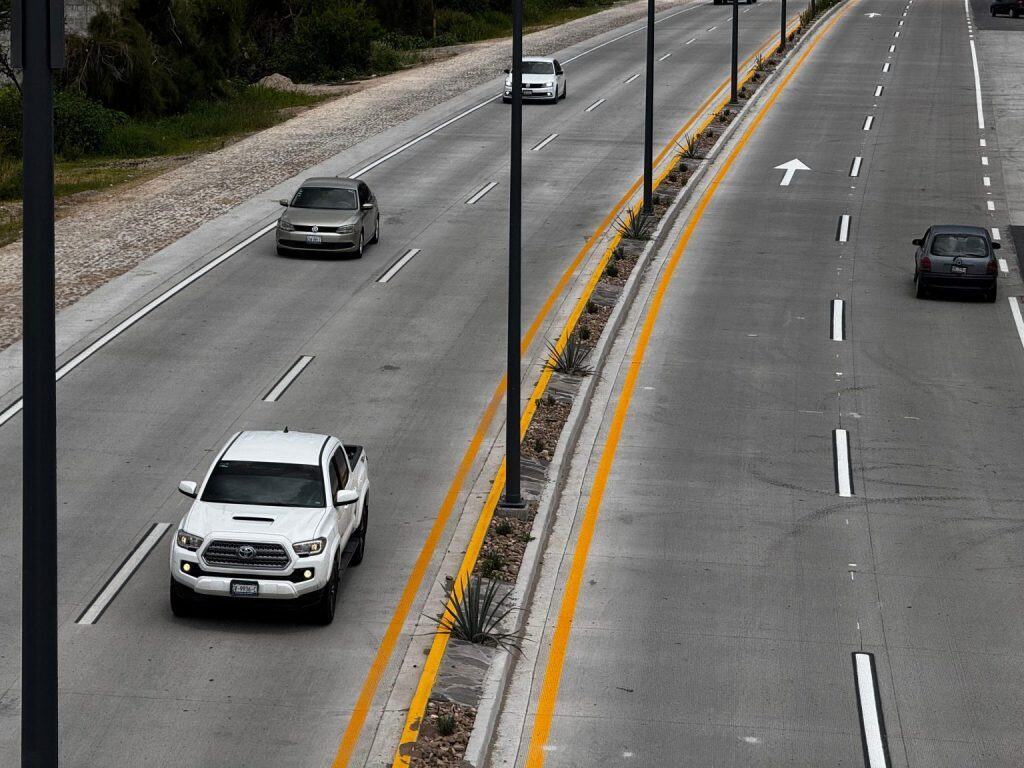 Autos circulando en una carretera con carril separado y señalización vial en la ciudad.