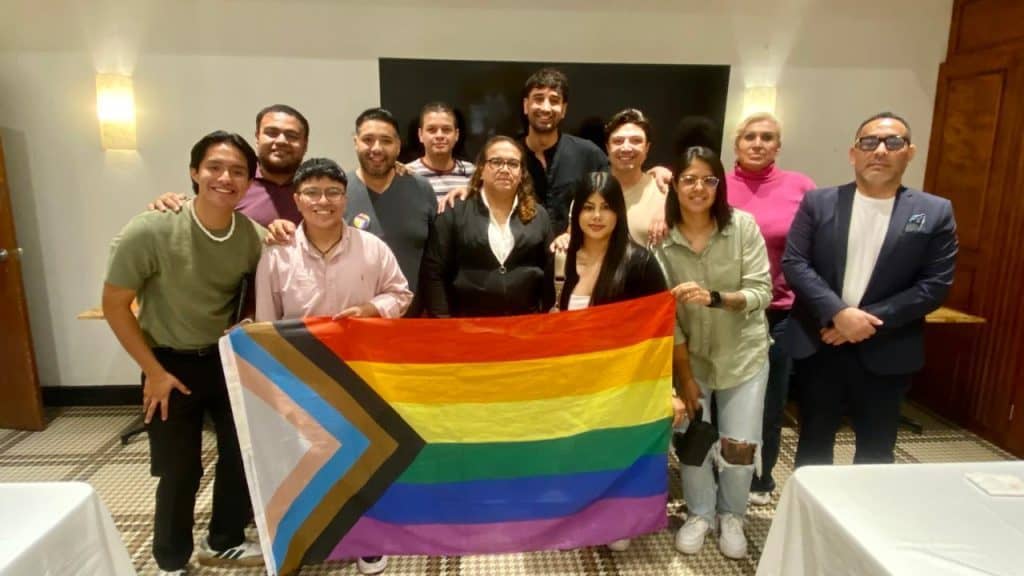 Personas en celebración del orgullo LGBTQ+ con bandera en salón de eventos, diversidad y derechos LGBTQ+ en México.