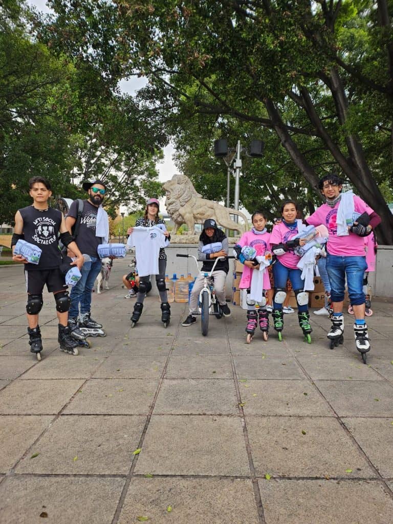Diversos jóvenes en patines y skateboards participando en actividad en parque con esculturas y áreas verdes.