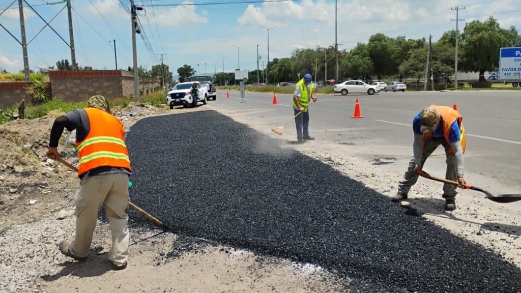 Trabajadores rehabilitando carretera con asfalto y señalización vial en ciudad, mantenimiento de calles urbanas, equipo de construcción y obra civil en acción.