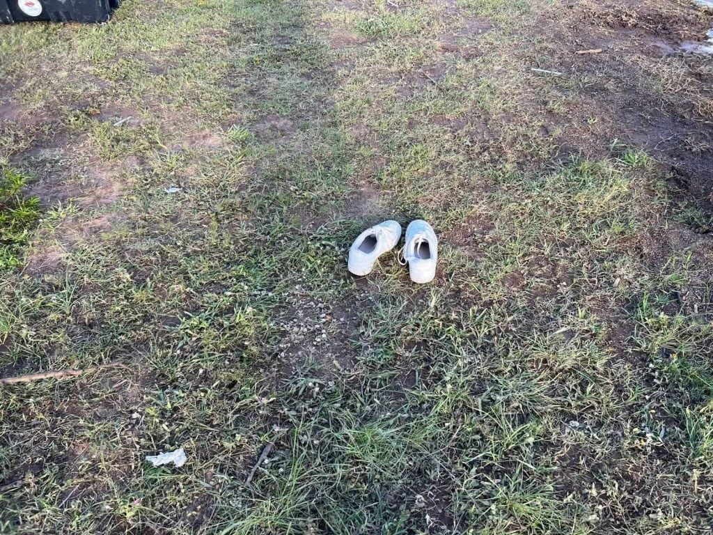 Zapatos blancos en césped con tierra, imagen de calle o parque en contexto rural o urbano.