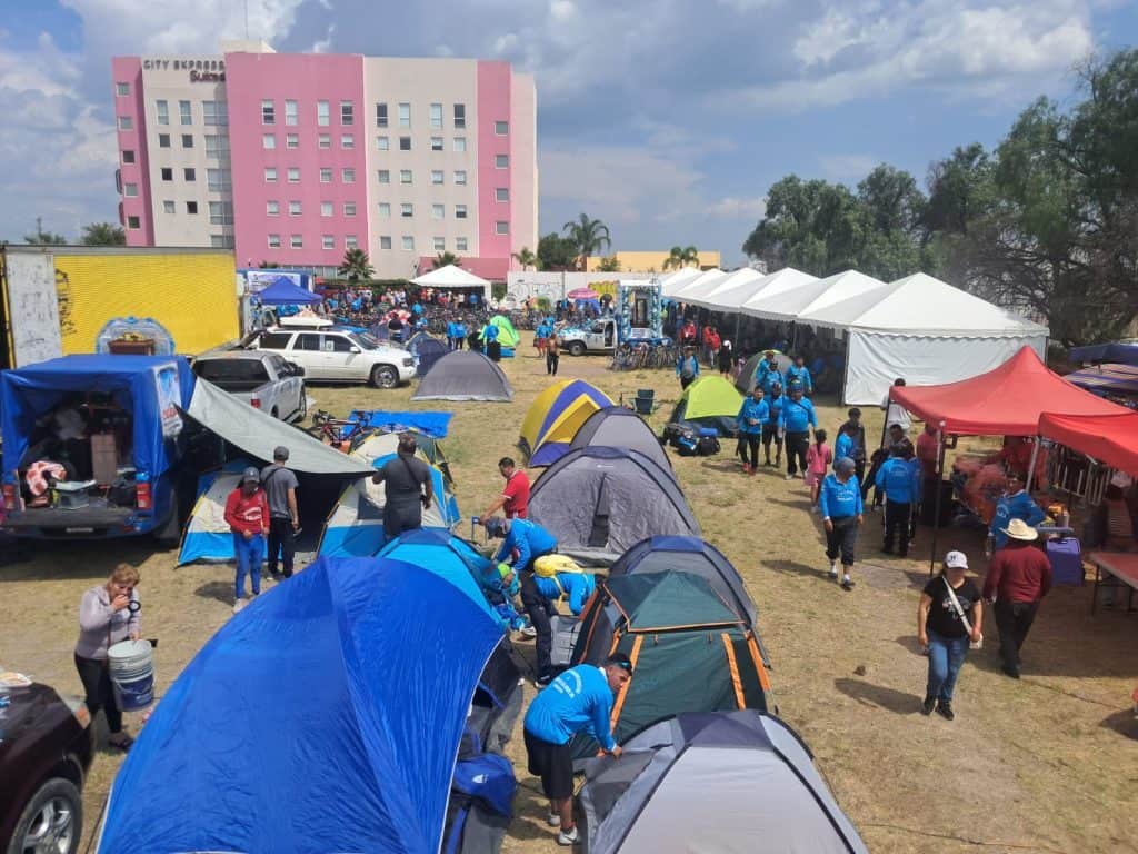 Alt: Encuentro comunitario con tiendas, carpas y asistentes en un espacio abierto en la ciudad.