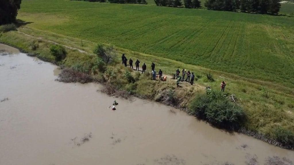 Tragedia en San Luis de la Paz: un menor pierde la vida tras caer en un bordo de agua Personas junto a río en campo agrícola, paisaje natural y actividades de pesca o exploración.