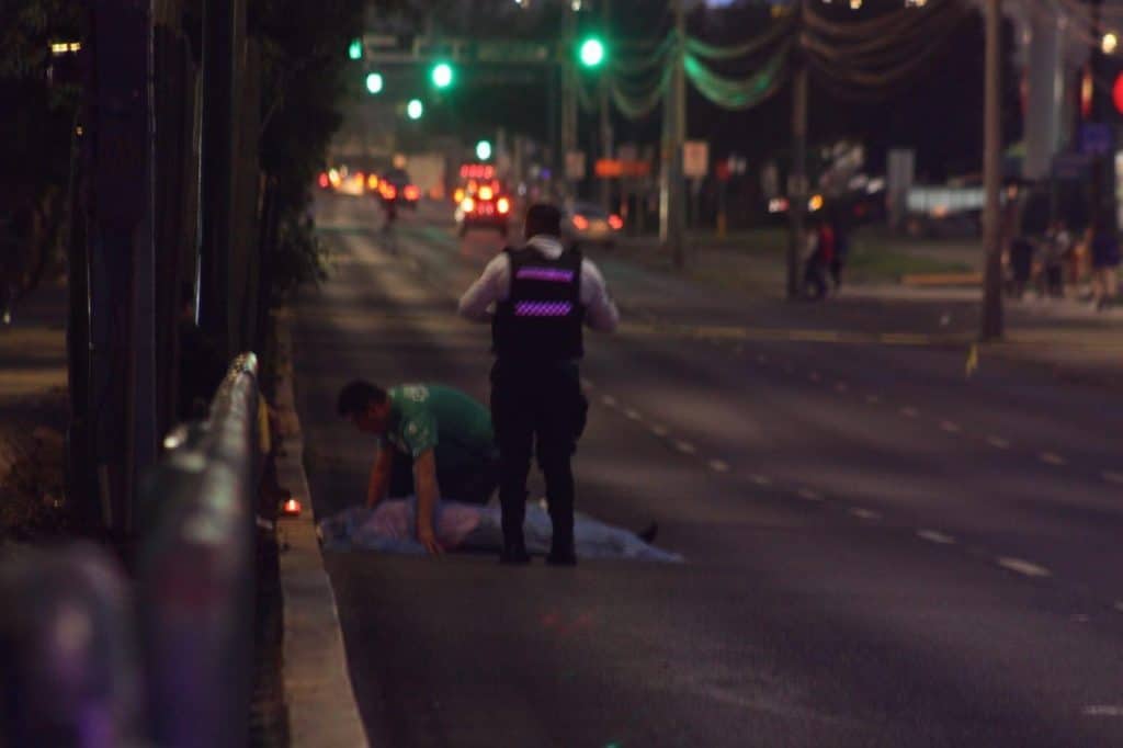 Accidente vial durante la noche en ciudad, paramédico atendiendo a víctima en la calle.