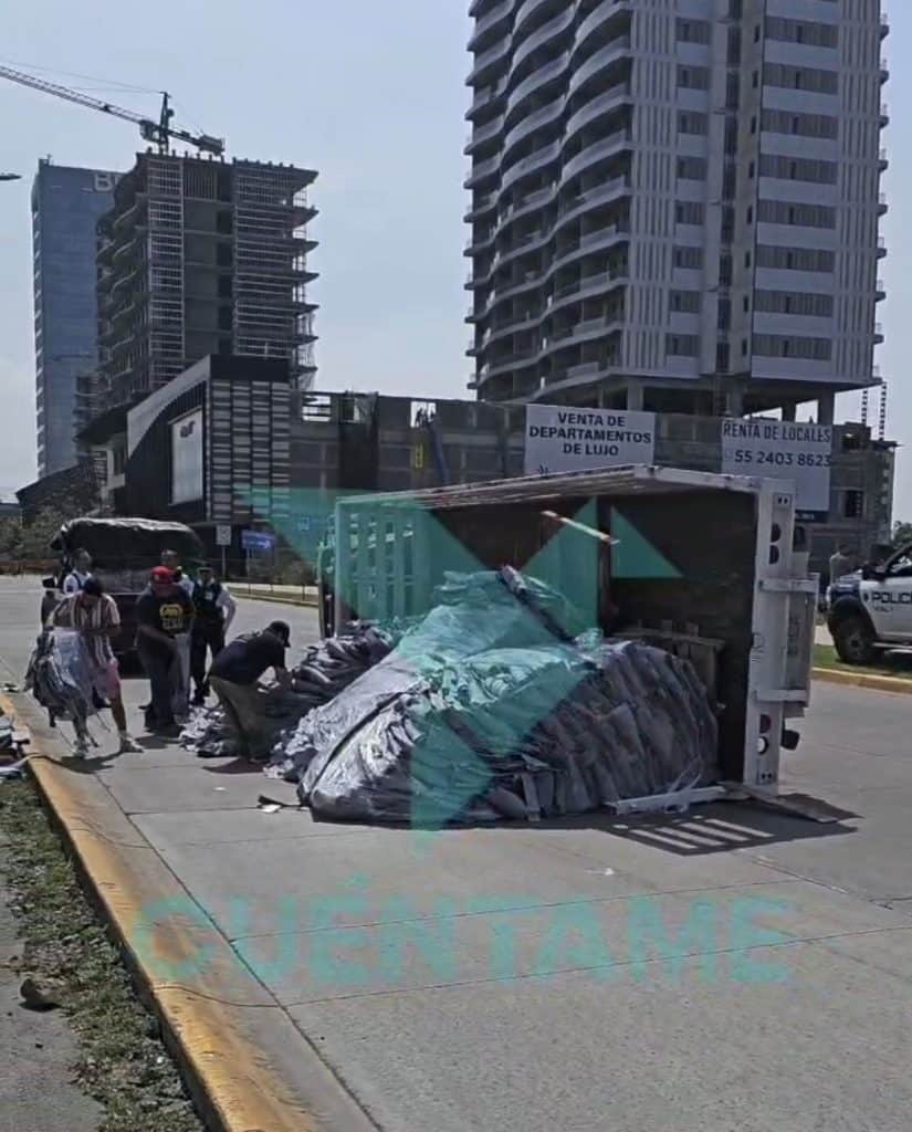 Contenedor de reciclaje volcándose en la calle en zona urbana con edificios altos al fondo.