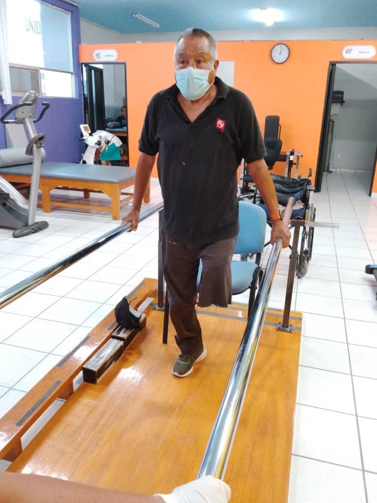 Paciente en rehabilitación con muletas y silla de ruedas en clínica de terapia física.