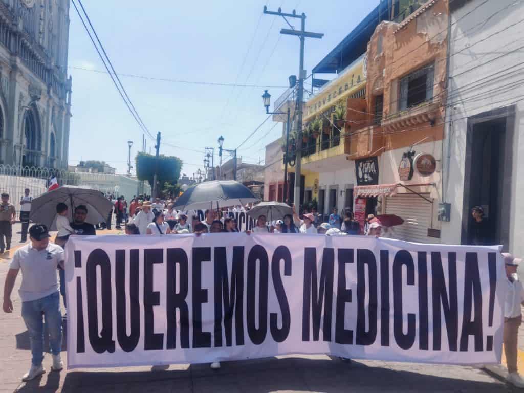 Ausencia de texto en la imagen, protagonizada por personas en marcha y con pancarta en una calle.