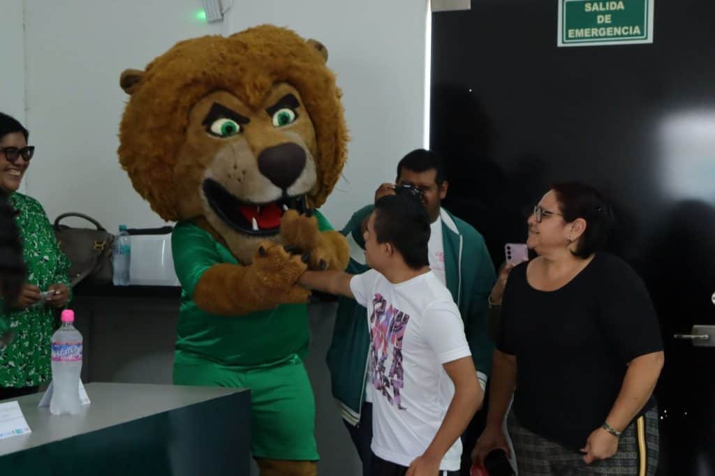 1. Persona disfrazada de león saludando a niños y adultos en evento escolar.