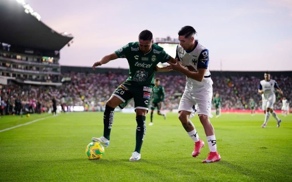 Jugadores de fútbol en un partido profesional en estadio lleno, disputando el balón con intensidad.