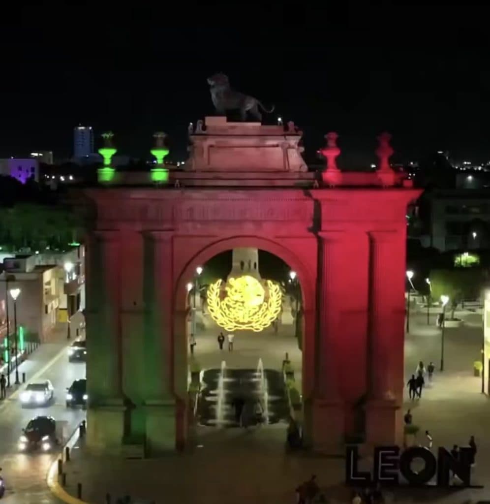 Majestuoso Arco de la Independencia en León, iluminado con luces verdes, rojas y amarillas en la noche.