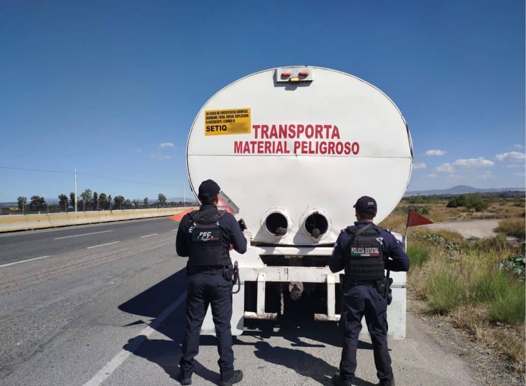 Camión de transporte de material peligroso en carretera con policías estatales presentes.