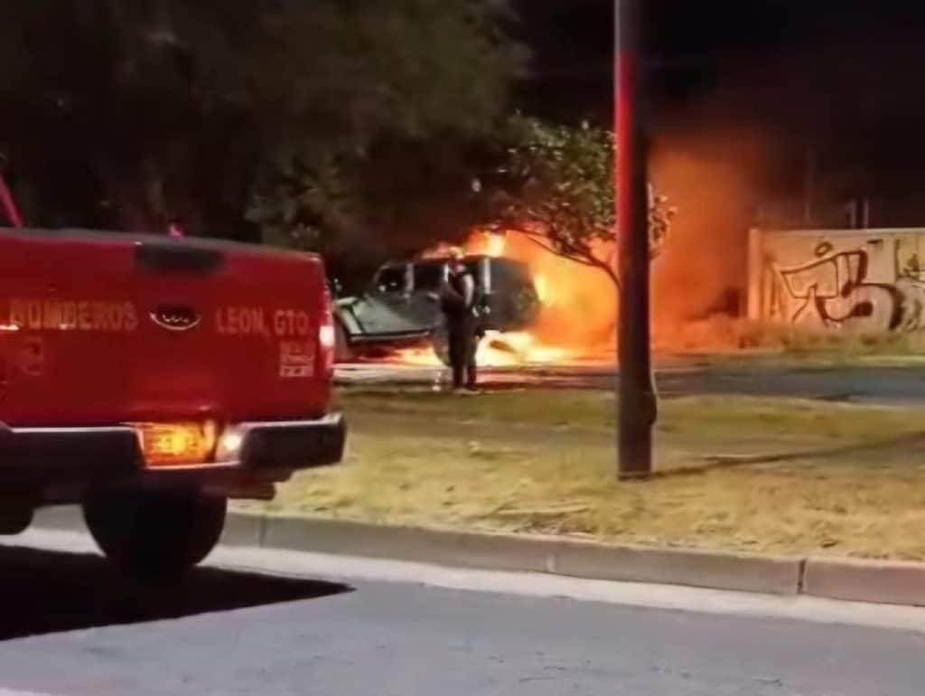 Vehículo en llamas durante emergencia de incendio nocturno en la calle, con elementos de rescate y advertencias.