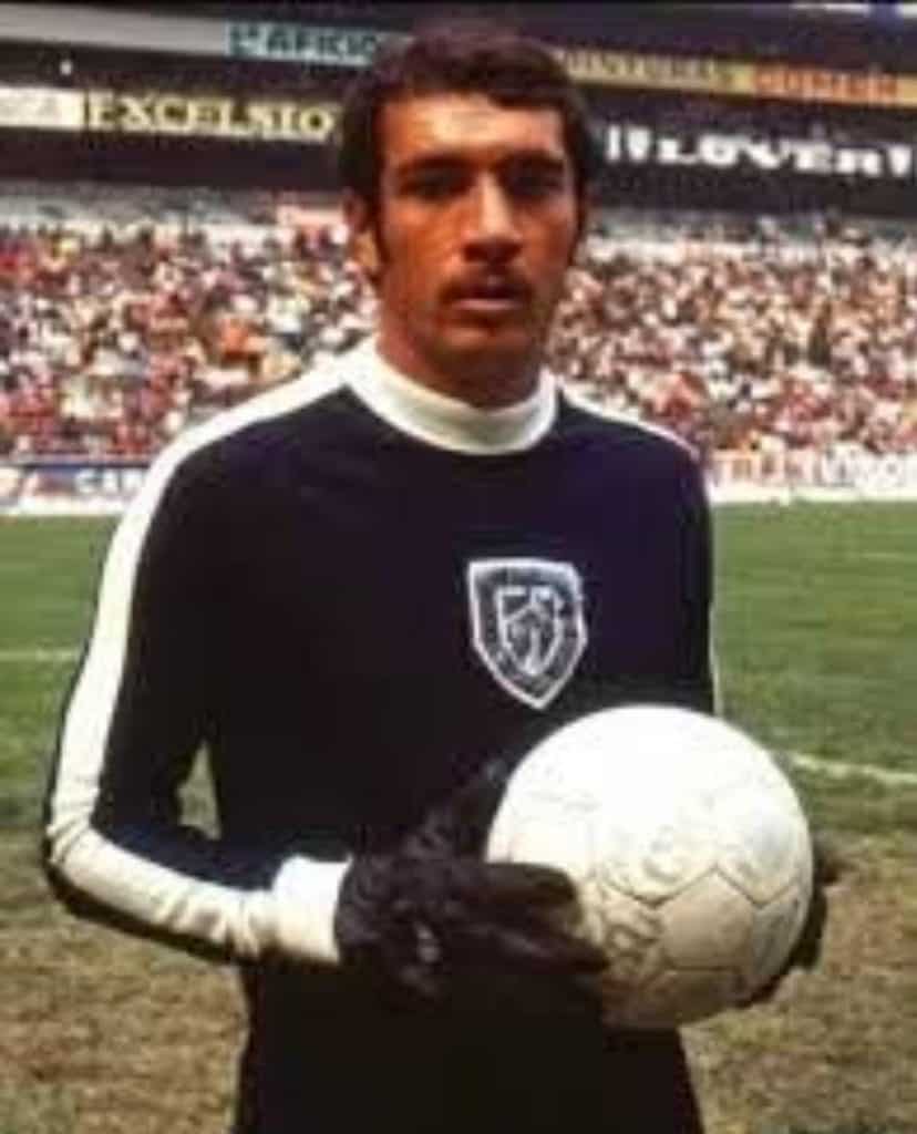 Golero de fútbol histórico, portando balón en estadio lleno de espectadores. Icono del deporte mexicano, uniforme negro con escudo.