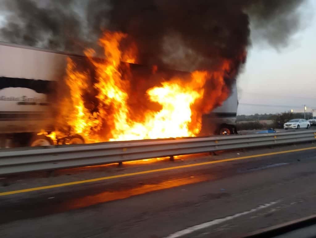 Incendio en autobús en la carretera, llamas y humo denso en medio del tráfico.