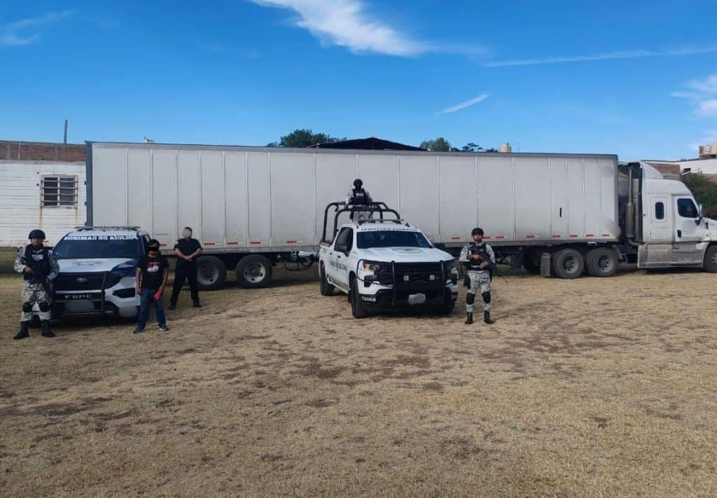 Recuperan tractocamión con mercancía extranjera valuada en cinco millones de pesos Muertos policía y militares en escena, junto a un camión grande en un terreno rural.
