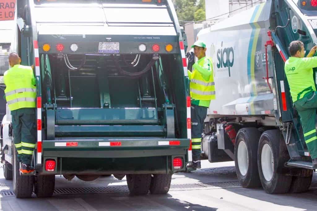 Camion de basura en acción, limpieza urbana, trabajadores en sitio, reciclaje y recolección de residuos.
