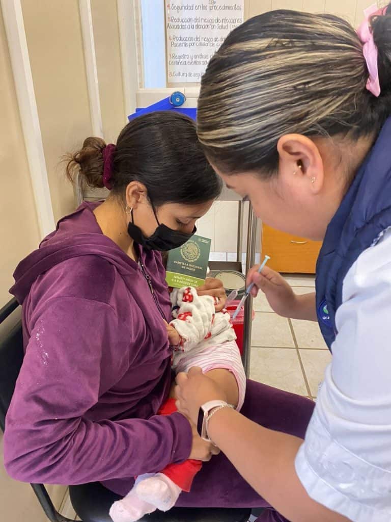 Vacuna a bebé en centro de salud, personal médico realizando vacunación infantil.