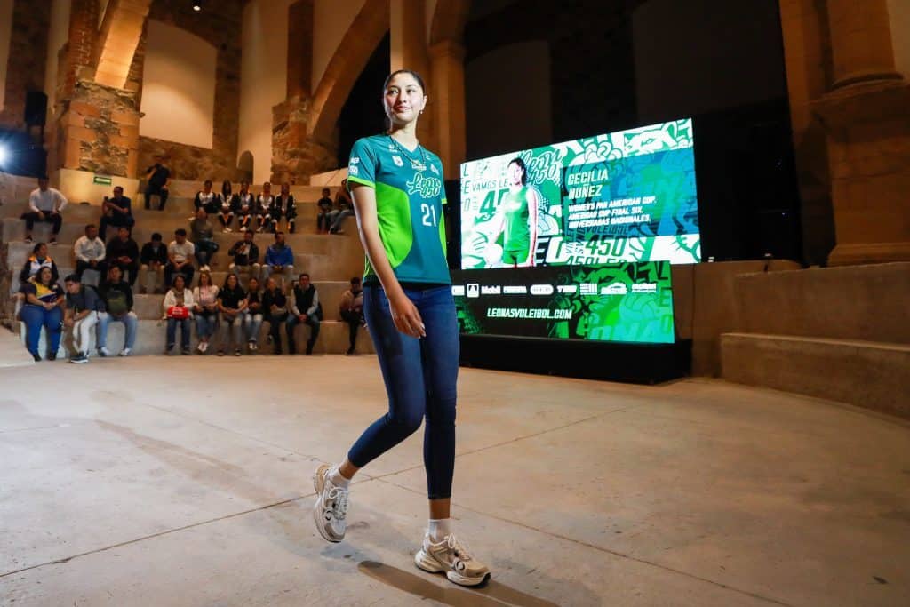 Juvenil jugadora de voleibol presentándose en evento con pantalla digital de fondo.