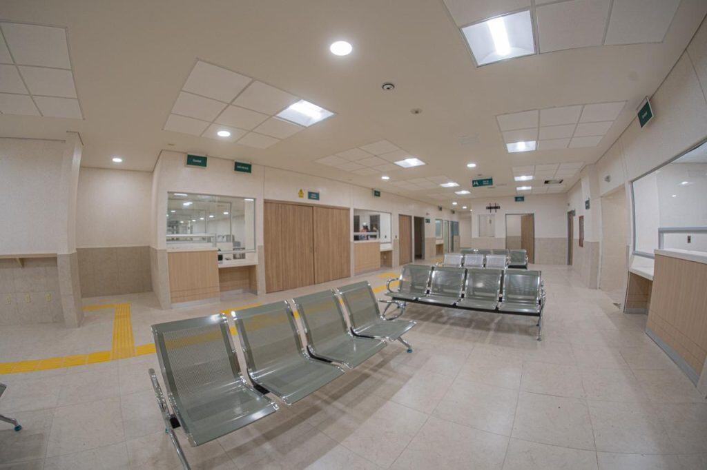 Puerta de hospital vacía con sillas de espera y señalización de emergencias.