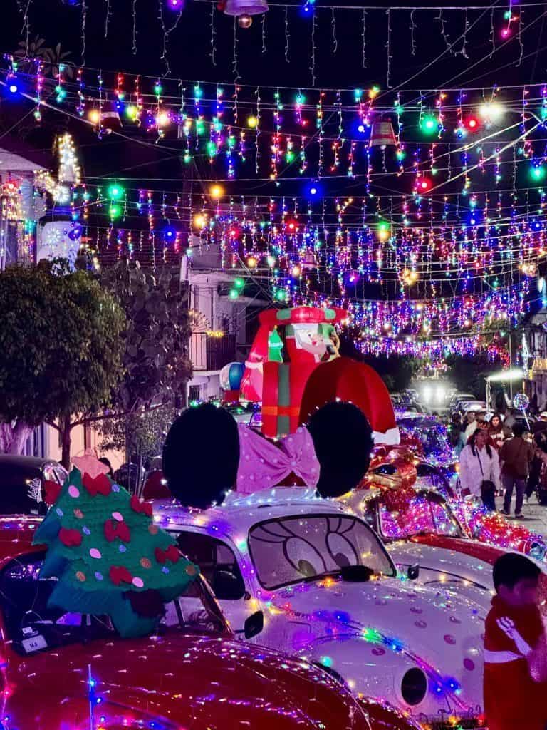 Luces navideñas en calles decoradas con autos decorados y personajes infantiles para celebrar Navidad con ambiente festivo.