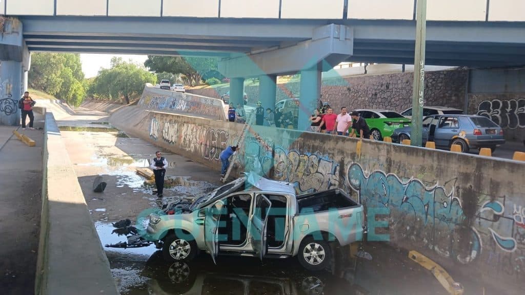 Accidente de auto bajo un puente, con varias personas y vehículos involucrados en la escena.