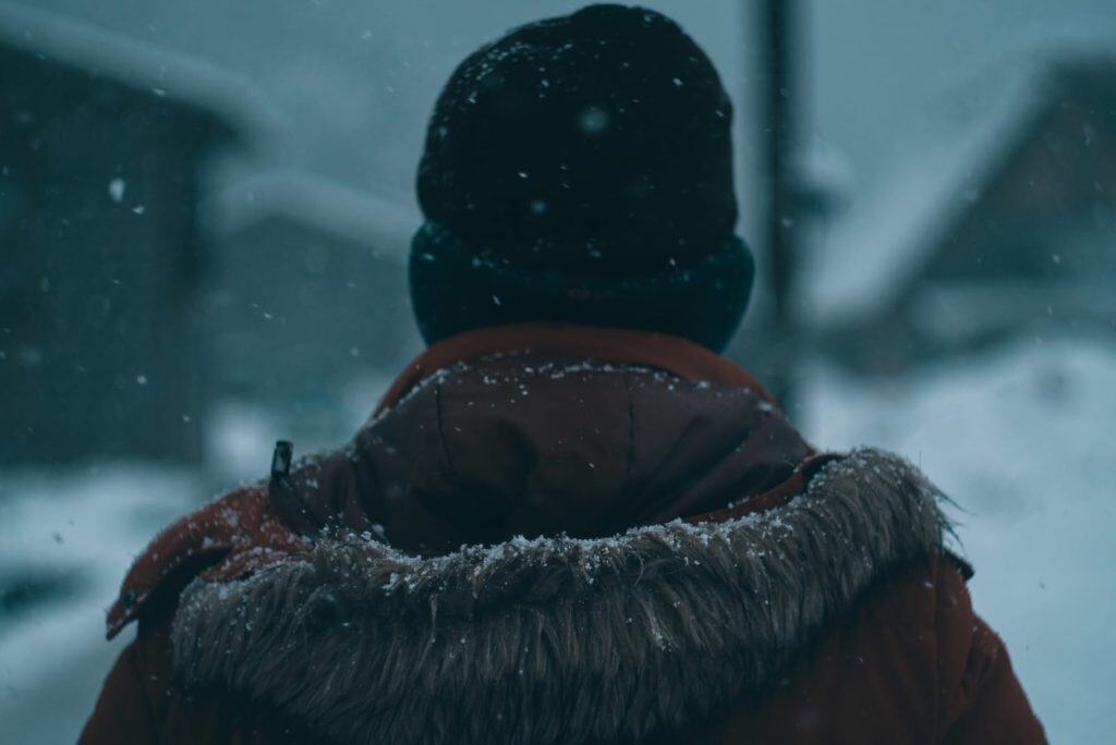 Hombre con abrigo y gorro en niebla invernal, ambiente frío y lluvioso en la ciudad.