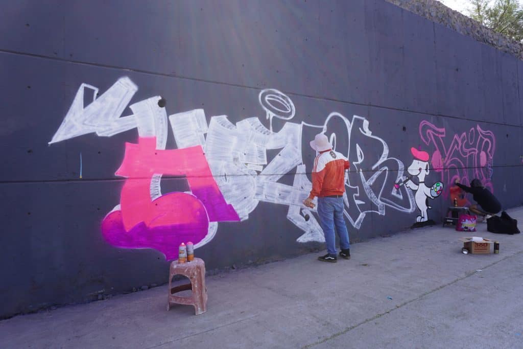 Colaboradores creando grafiti con pintura en una pared urbana, arte callejero, mural colorido y expresión artística en Ciudad.