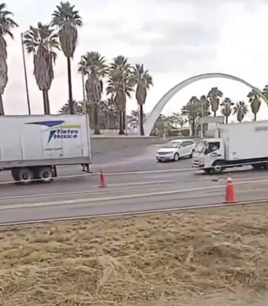 Camiones y autos en la autopista con palmeras y arco en fondo, vista urbana de Los Ángeles.