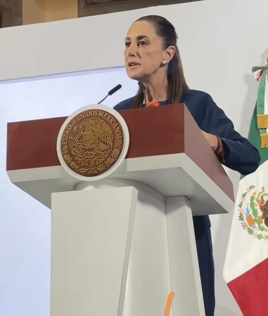 Paisaje de una mujer en discurso en podio con escudo de México y bandera nacional, con enfoque en política y liderazgo.