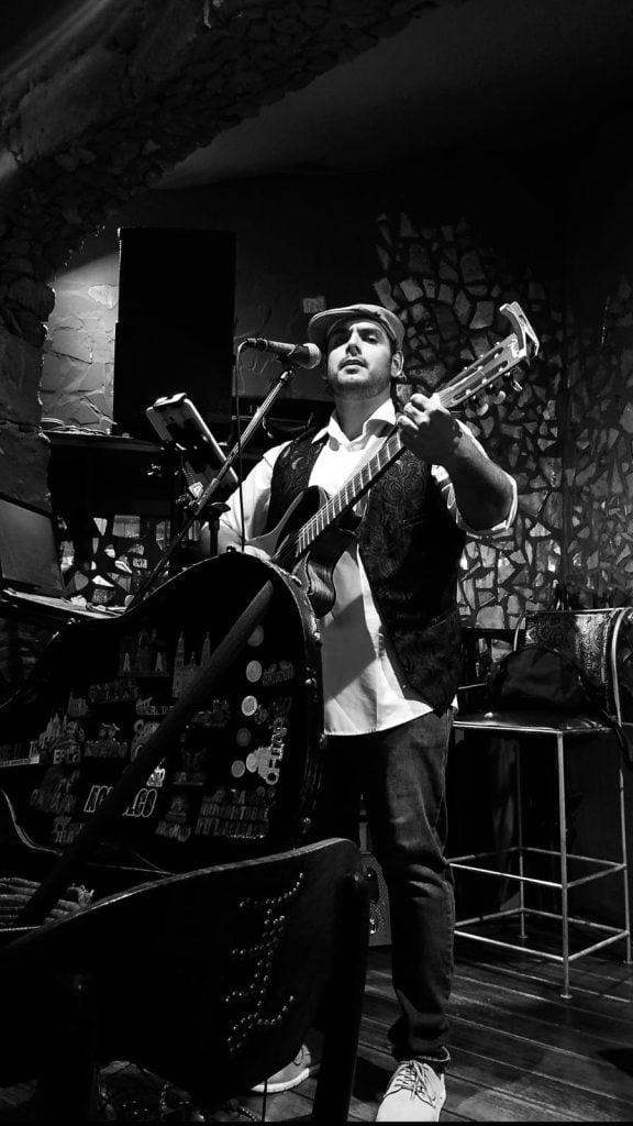 Carlo Stefano: el sanmiguelense que quiere rescatar la música con sentido y devolverle a México sus canciones más valiosas 1. Un músico tocando guitarra en un escenario de jazz en un bar con decoración de piedra.