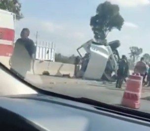 Camión de carga pierde el control e invade carril contrario en la León–Lagos; chofer resulta lesionado Accidente de coche volcado en la carretera con humo y personas observando.