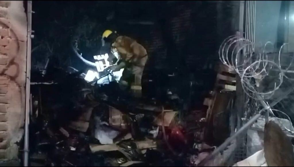 Un bombero inspecciona los restos de un incendio en un local comercial en la noche.