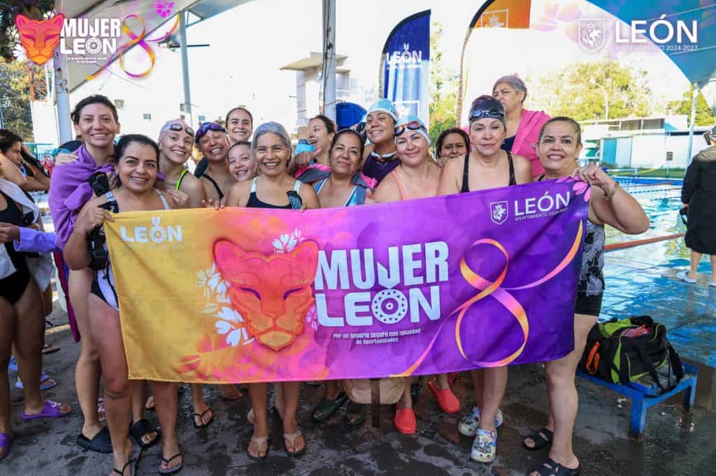 Mujeres en la piscina con bandera "Mujer León", promoviendo igualdad y deporte femenino en León, Guanajuato.