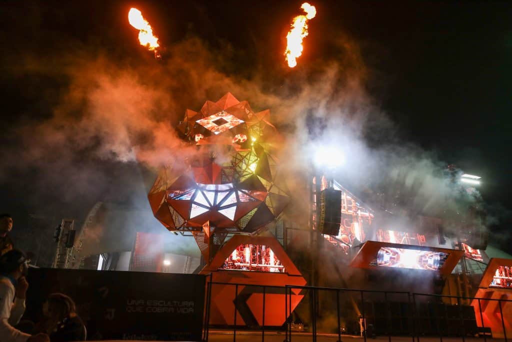 Fondo de escenario de festival con iluminación y humo, tecnología y arte en un evento nocturno.