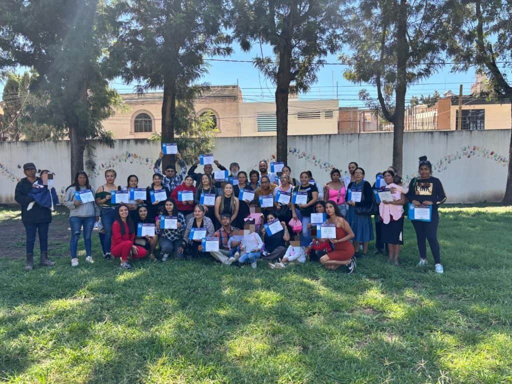 Más de 790 personas fortalecen sus habilidades parentales Grupo de personas en un evento al aire libre, celebrando con certificados y sonrisas, en un ambiente comunitario y festivo.