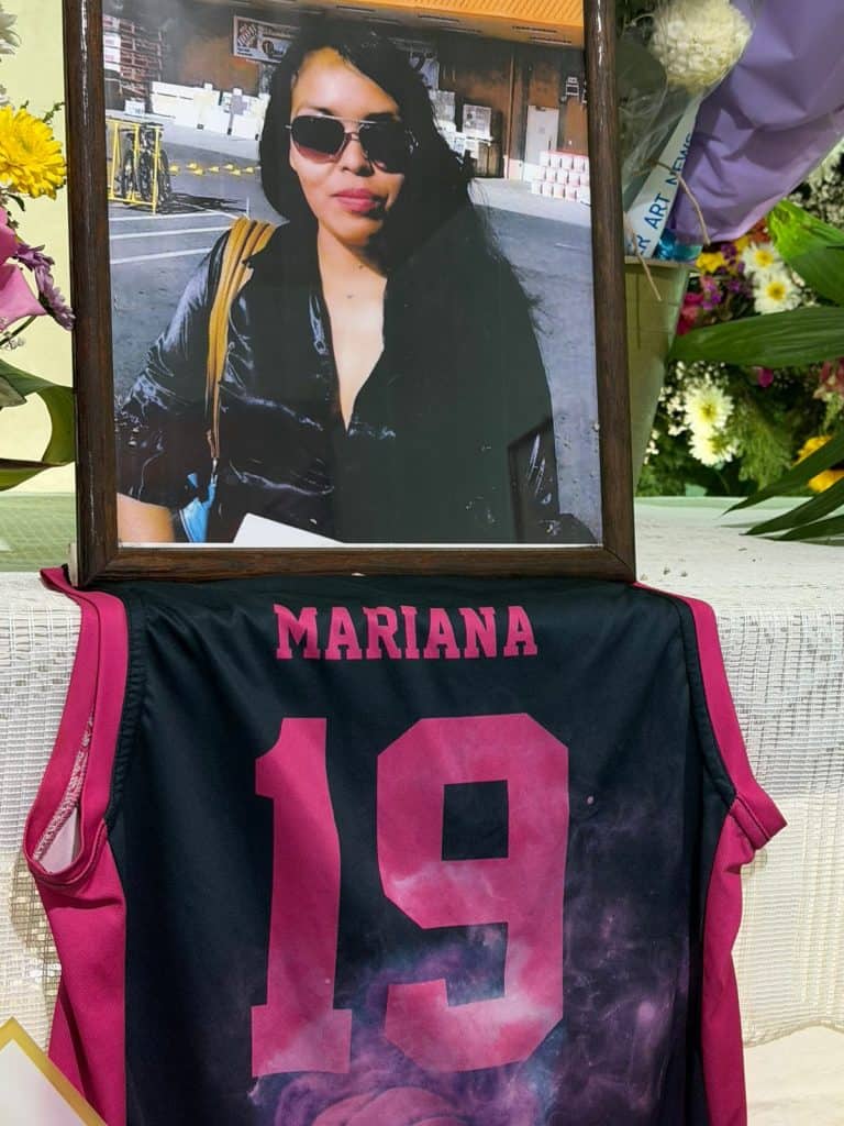 Foto de homenaje a Mariana en un funeral, con su camiseta de fútbol y un retrato enmarcado en un altar floral.