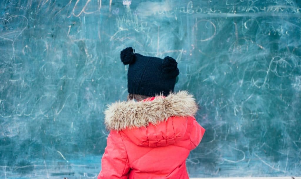 Niño con abrigo rojo y gorro con orejas en pizarra con escritura.