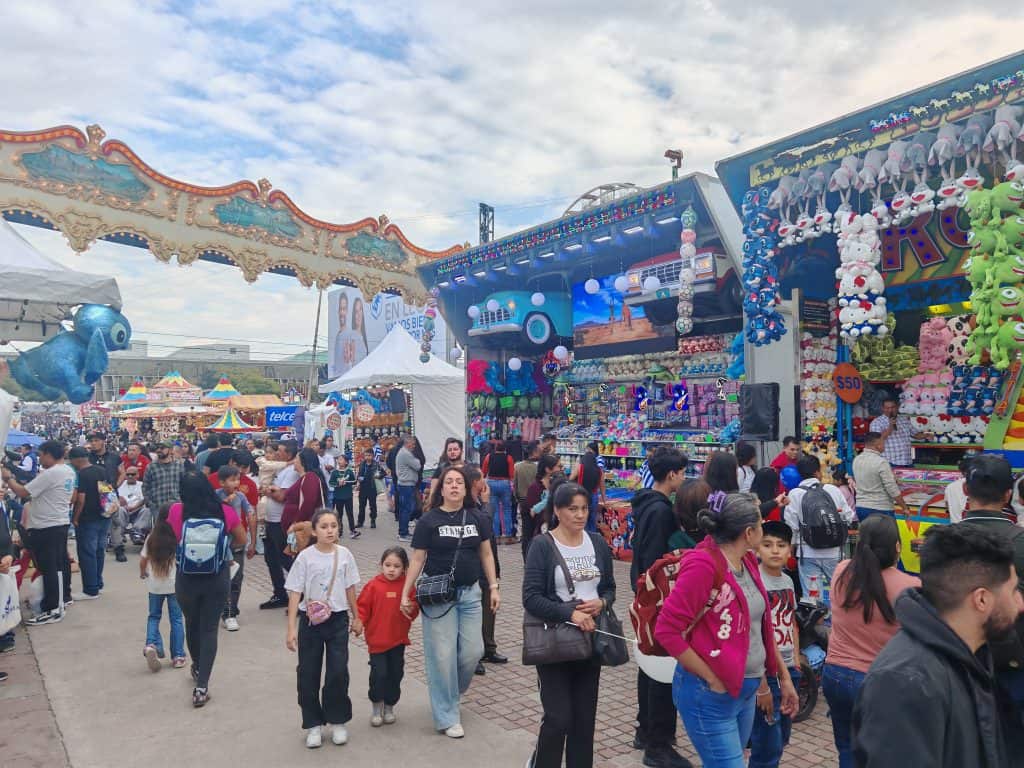 Colorido parque de feria con juegos, puestos y gente disfrutando en un día soleado en México.