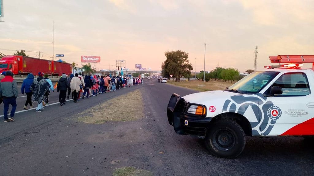 Personas haciendo fila en la carretera en presencia de una unidad de protección civil, en un contexto de movilidad y seguridad.