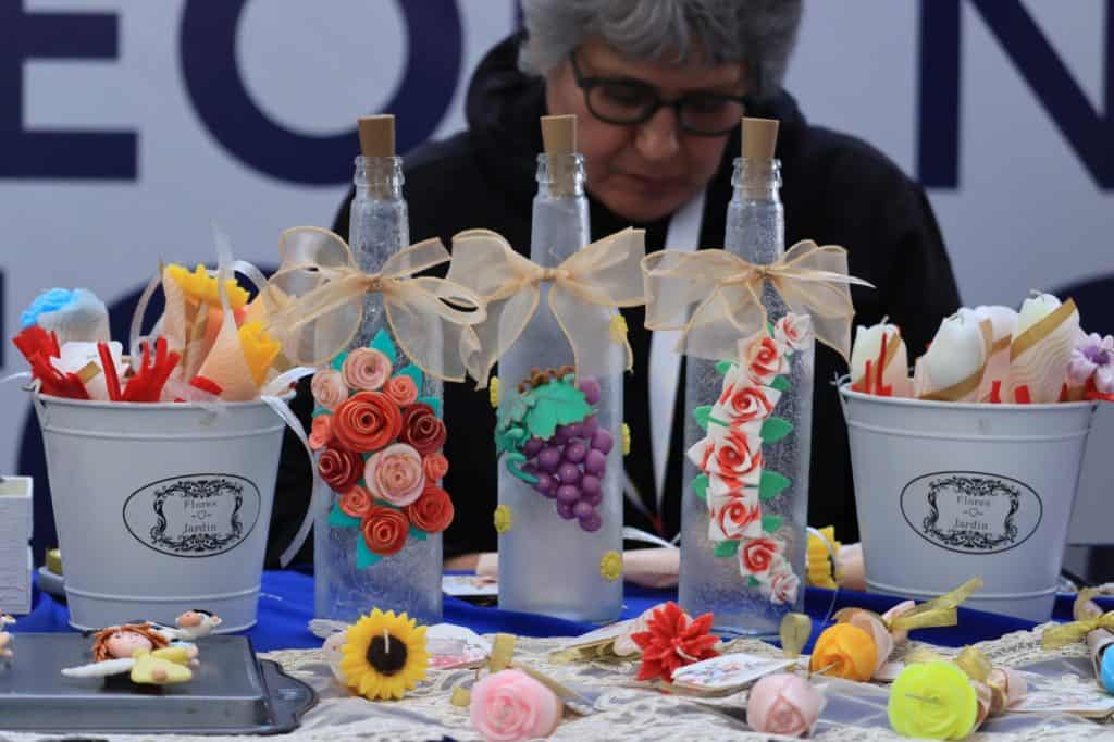 Diversa decoración de flores y botellas decorativas hechas a mano en stand de feria artesanal.