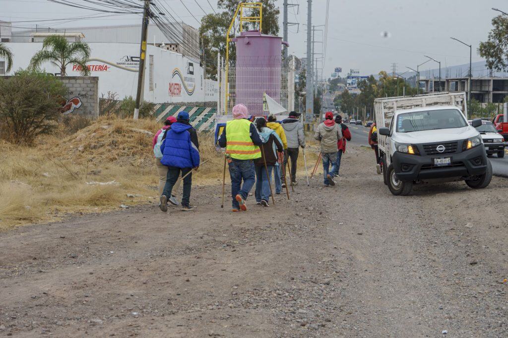 Personas caminando en calle de tierra en zona urbana con herramientas de ayuda para personas con discapacidad.
