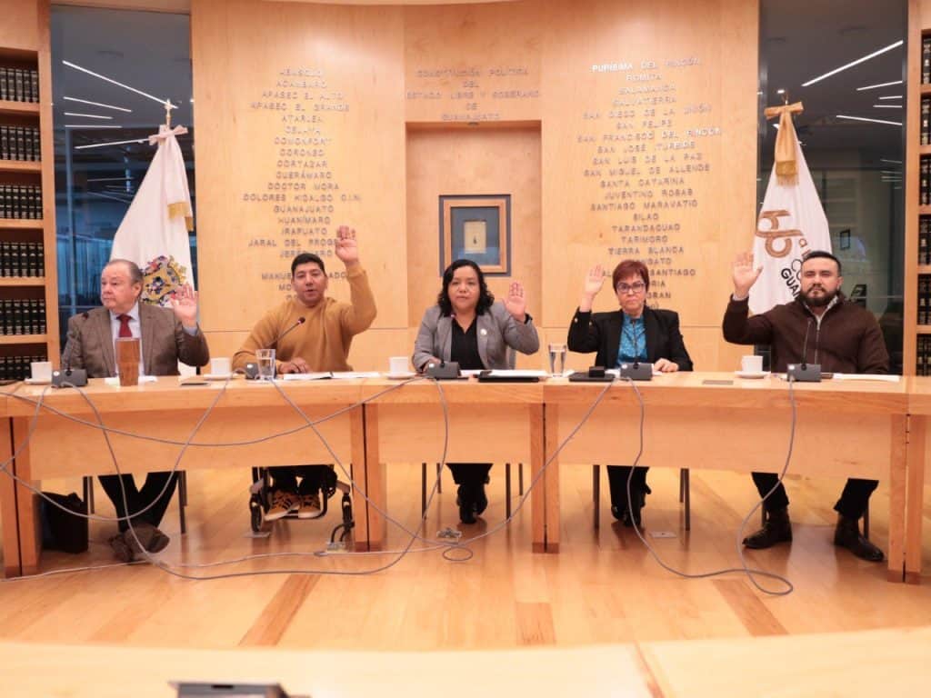 Representantes en reunión oficial en un entorno institucional, levantando mano en señal de voto o acuerdo.